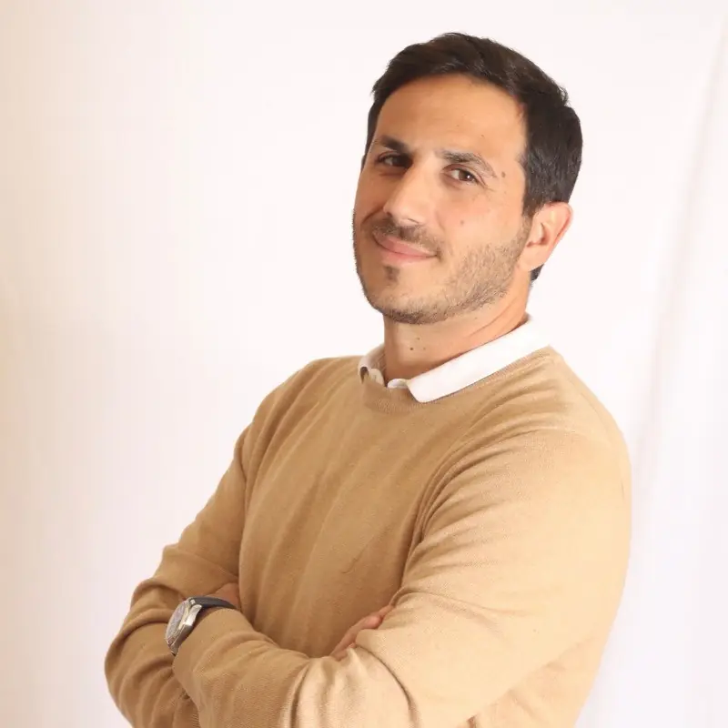 Portrait d'Anthony Israel Aiache, fondateur d'IsraBible, souriant, bras croisés, pull beige