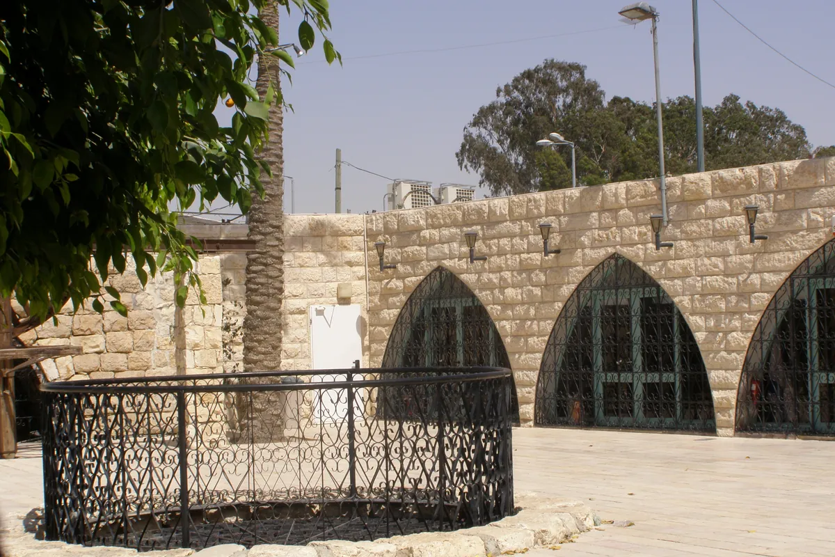 Round well-head behind a railing, in front of an arcaded stone building in the old city of Beersheba