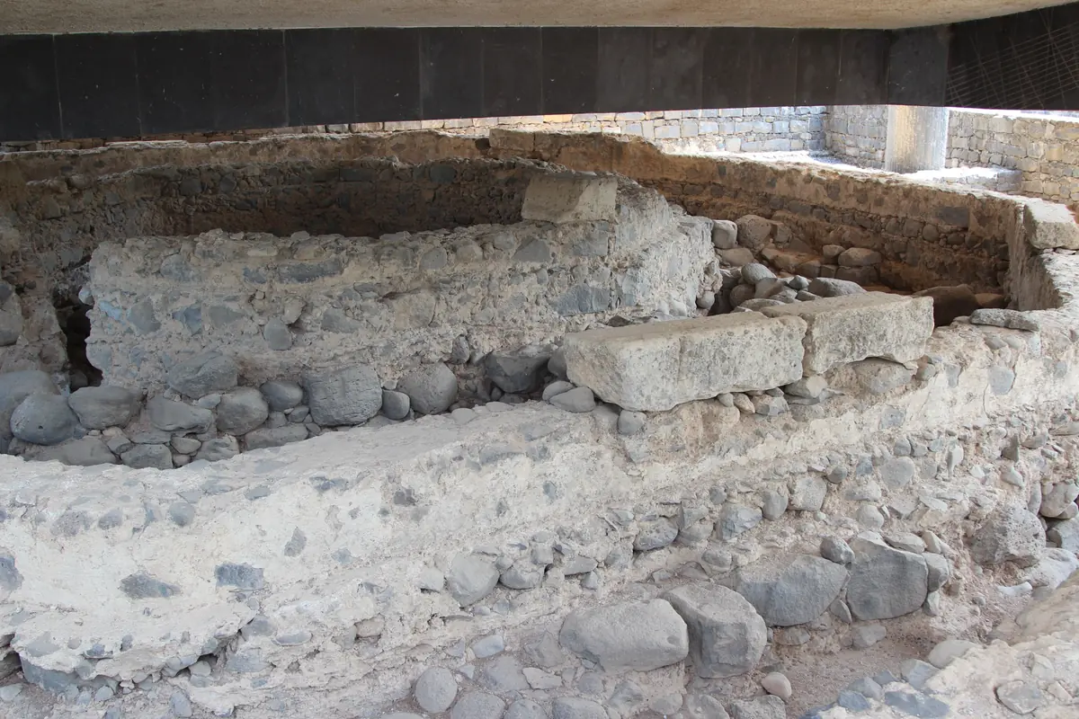 קירות מאבנים אפורות ומאבני בזלת מעוגלות, שרידי בית עתיק המוגנים תחת תקרת בטון