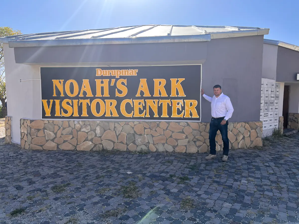 A low building with a large sign reading "Durupinar Noah's Ark Visitor Center" and a man standing beside it