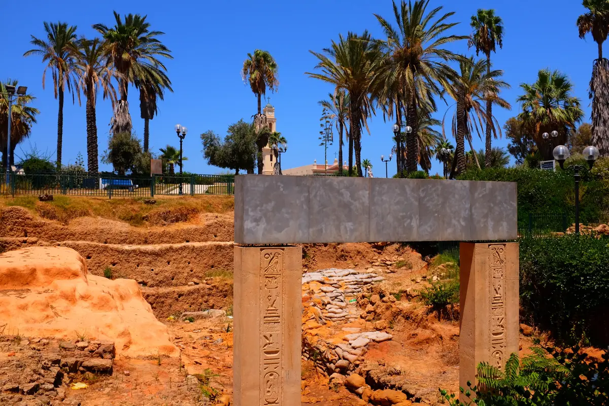 שחזור של שער אבן מלבני חרוט בכתב חרטומים, מעל אזור חפירה בצבע אוקר, ודקלים ברקע