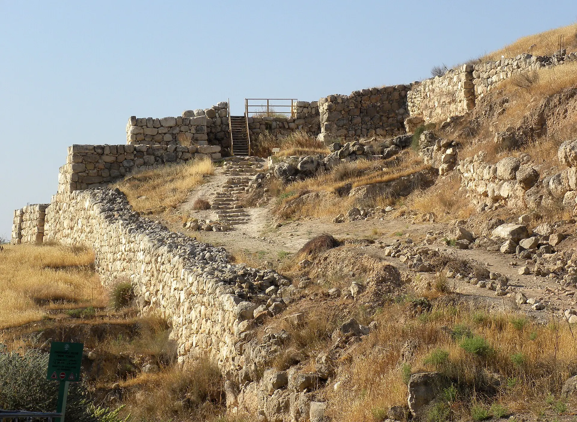 חומת אבן ושביל מדרגות העולה אל שער העיר בתל לכיש, על מדרון של עשב יבש