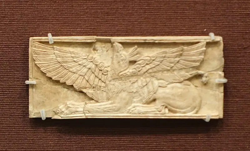 Ivory plaque carved in relief with a crouching griffin with outspread wings, on a red background