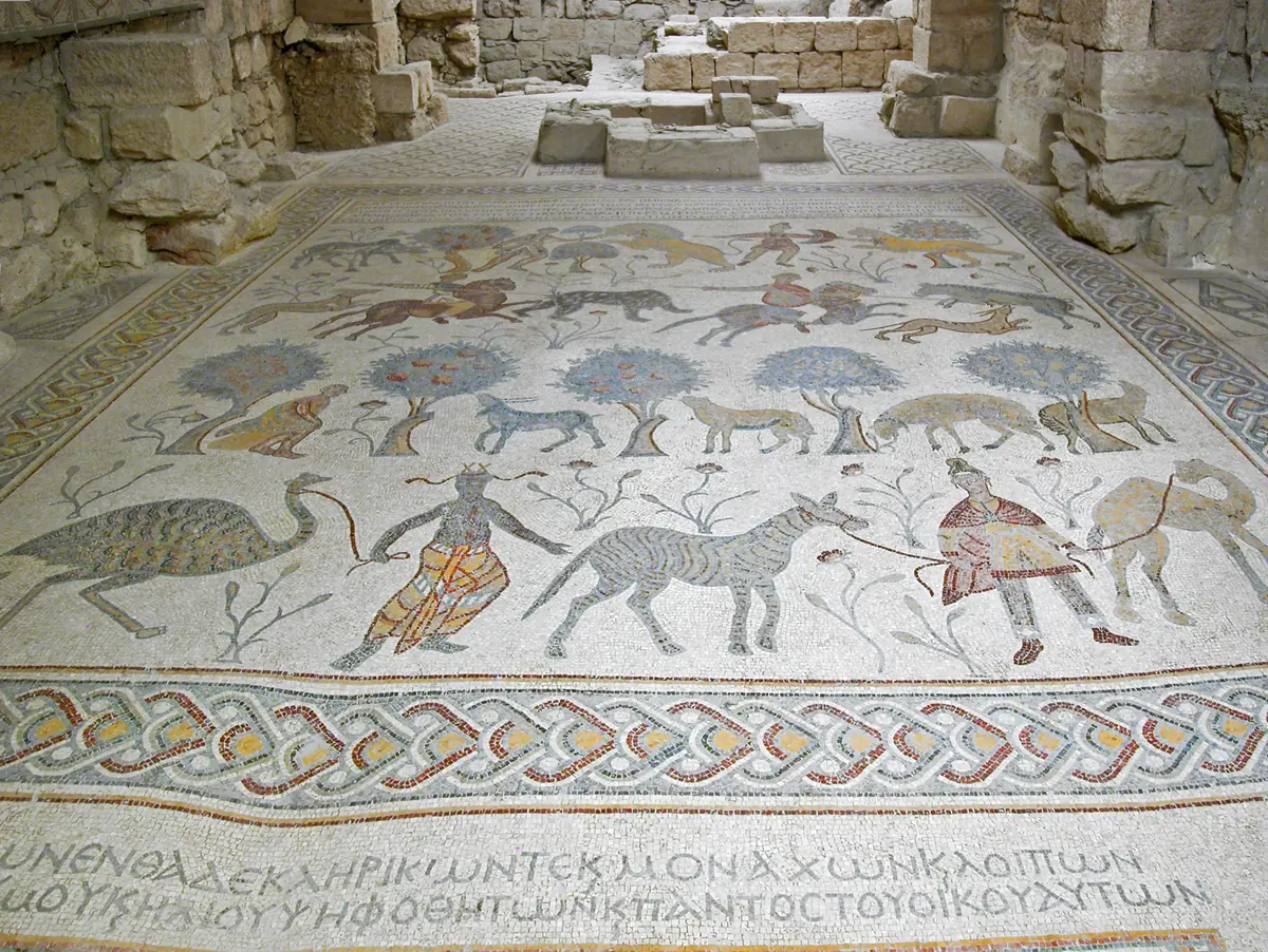 Pavement de mosaïque avec des cavaliers, des arbres, une autruche, un zèbre et un chamelier, bordé d'une inscription grecque