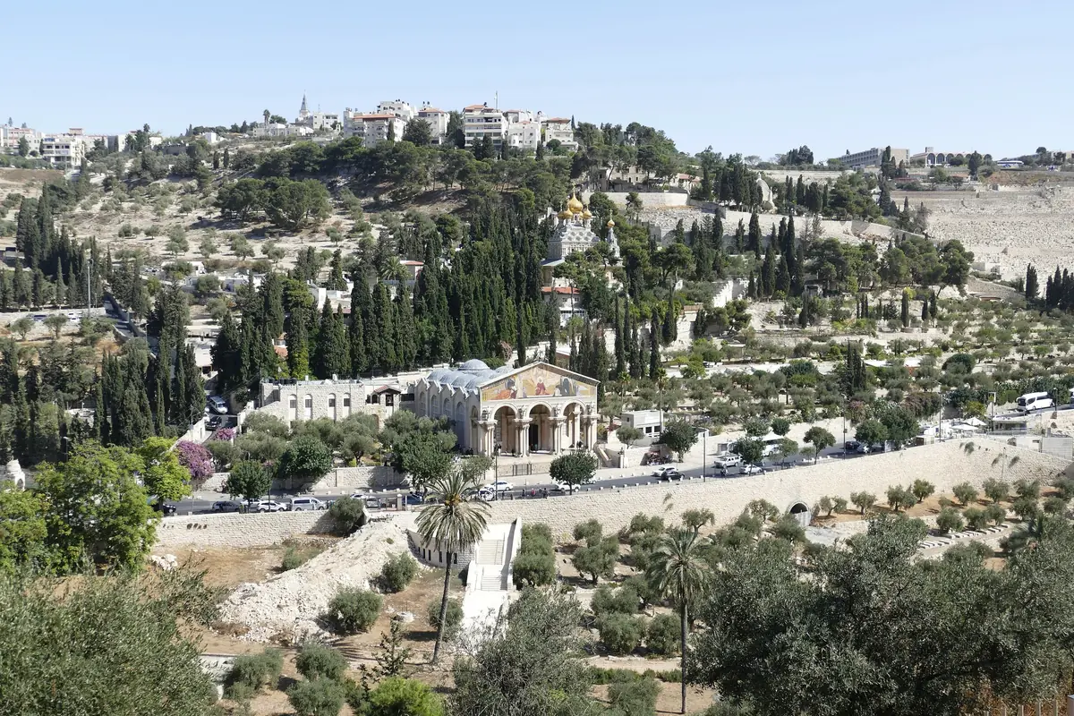 Slope of the Mount of Olives with the mosaic façade of the Church of All Nations in the foreground, the gilded onion domes of a Russian church among cypress trees and the cemetery on the right