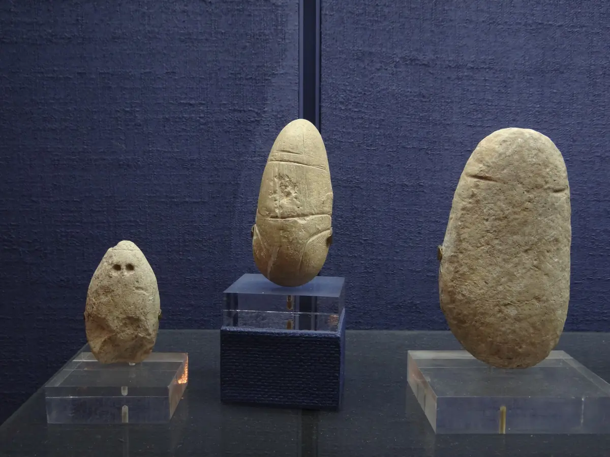 Trois galets de calcaire gravés de traits figurant un visage, posés sur des supports d'exposition au musée de Sha'ar HaGolan