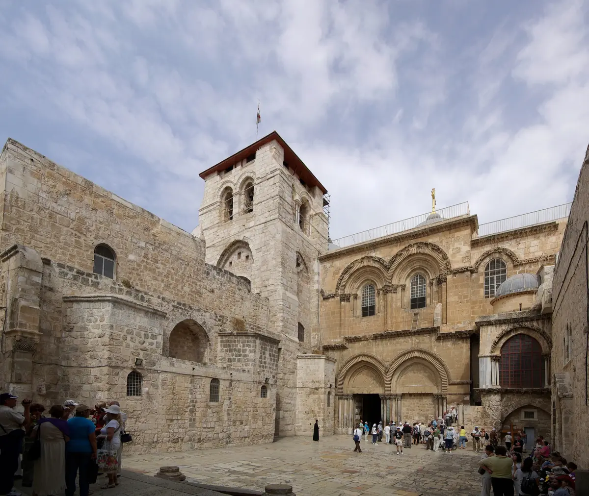 החזית הרומנסקית של כנסיית הקבר מאבן בהירה עם מגדל הפעמונים, הרחבה ובה מבקרים, וסולם קטן מתחת לחלון בקומה העליונה