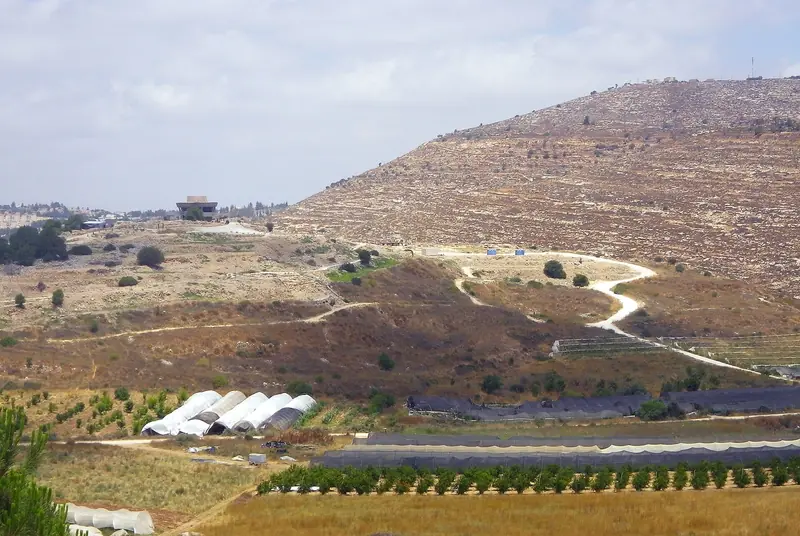 גבעת תל שילה ועליה שבילים ושרידים, ובראשה מבנה עגול, למרגלות הר מדורג