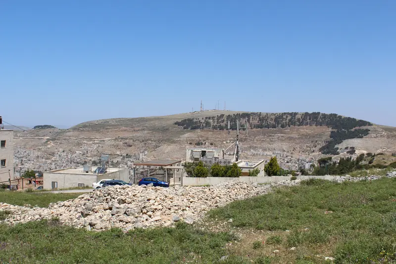 הר עיבל, גבעה חשופה שעל ראשה אנטנות ובשוליה אורנים, מעל בתי שכם