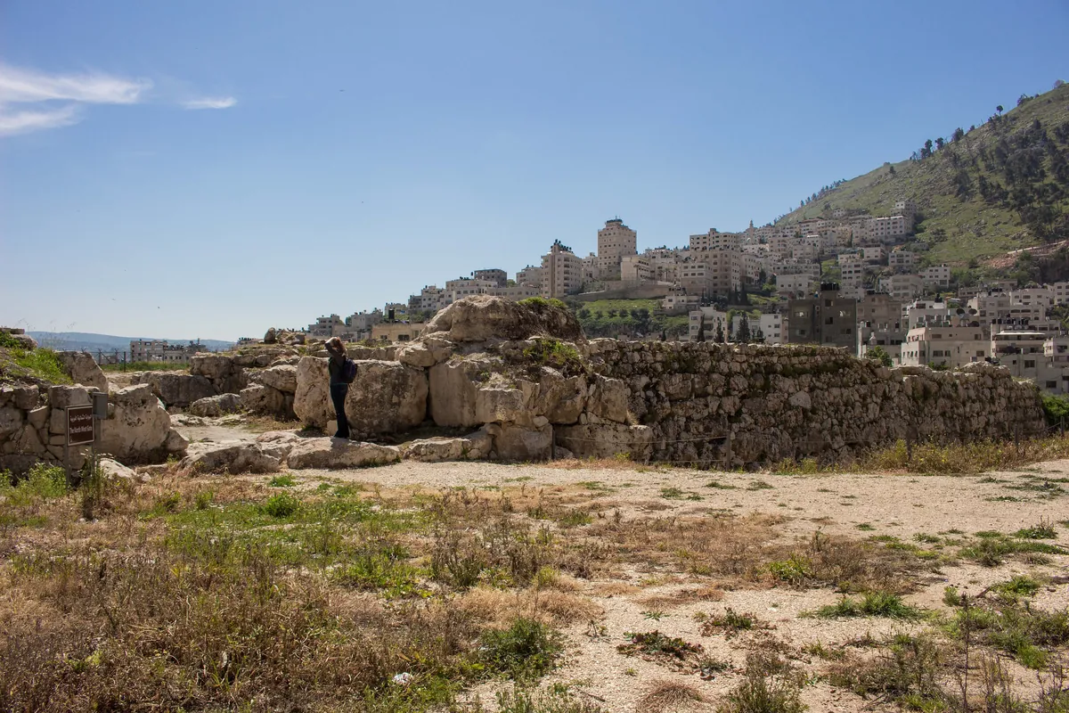 Excavated stone walls of Tell Balata, with the houses of Nablus on the hillside