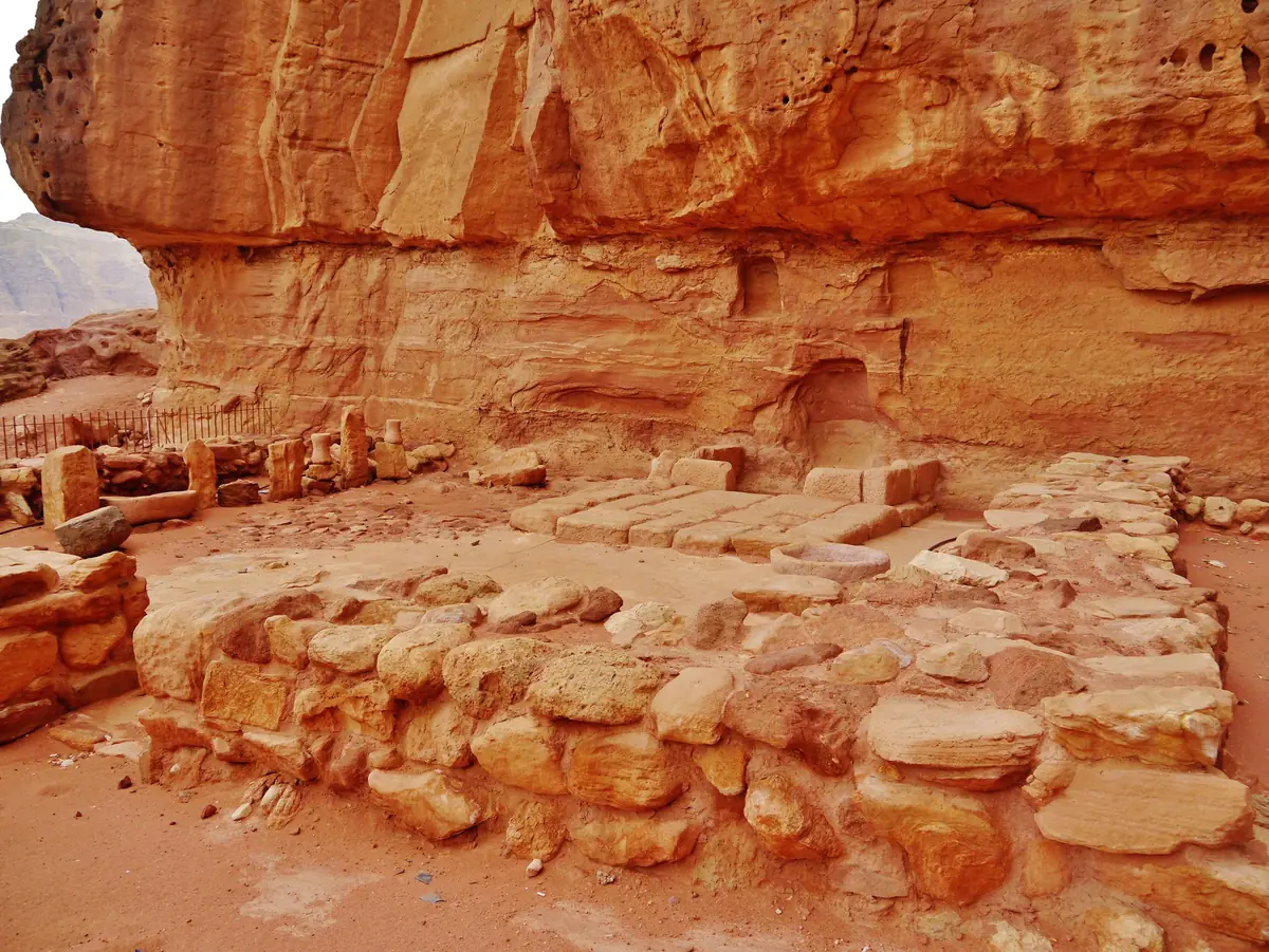 Low stone walls of a small shrine at the foot of a red sandstone cliff